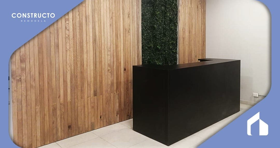 Recepción con mostrador negro, muro con acabado de madera y una franja vegetal vertical.