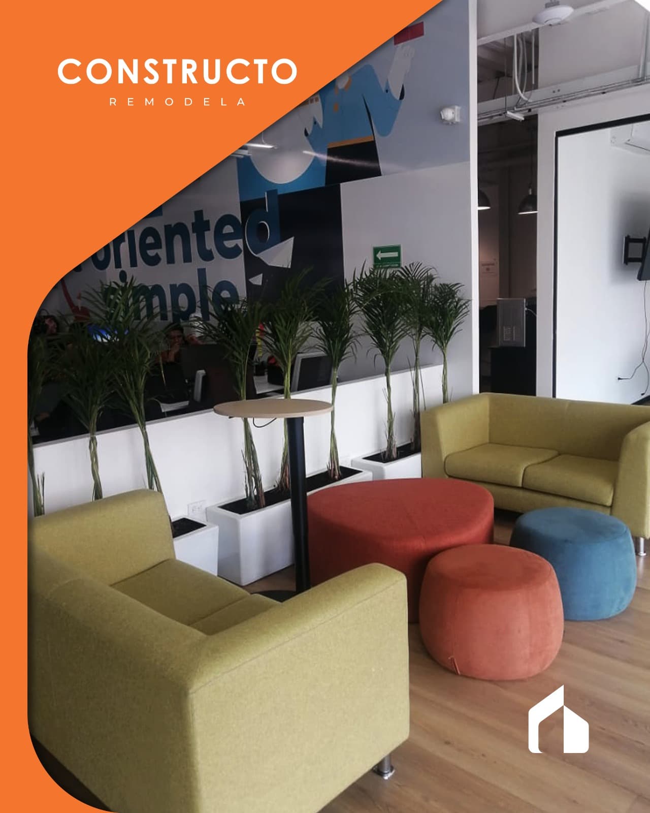 Sala de espera con sillones verdes, asientos de colores y jardineras frente a una división de vidrio.